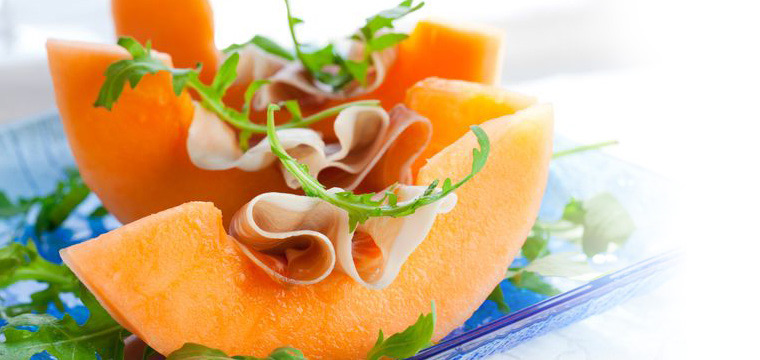 Postre de catering con rodajas de melón, embutidos y rúcula